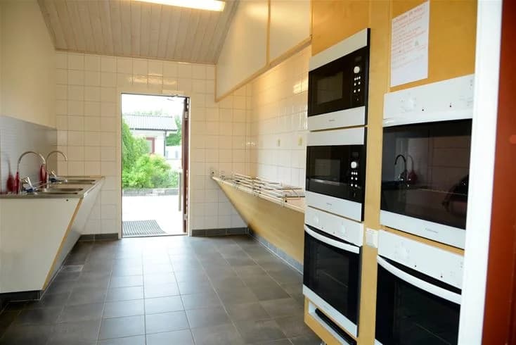 Ett modernt kök på Gullbrannagården med stilren inredning. Bilden visar ett kök med kaklade väggar och golv, stora köksapparater och skinande vita skåp.