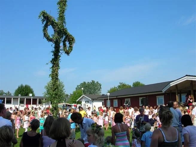 En livlig scen på Gullbrannagården med människor i olika åldrar som deltar i ett offentligt evenemang. Deltagarna njuter av fritidsaktiviteter och det råder en känsla av gemenskap och nöje i vårvädret.