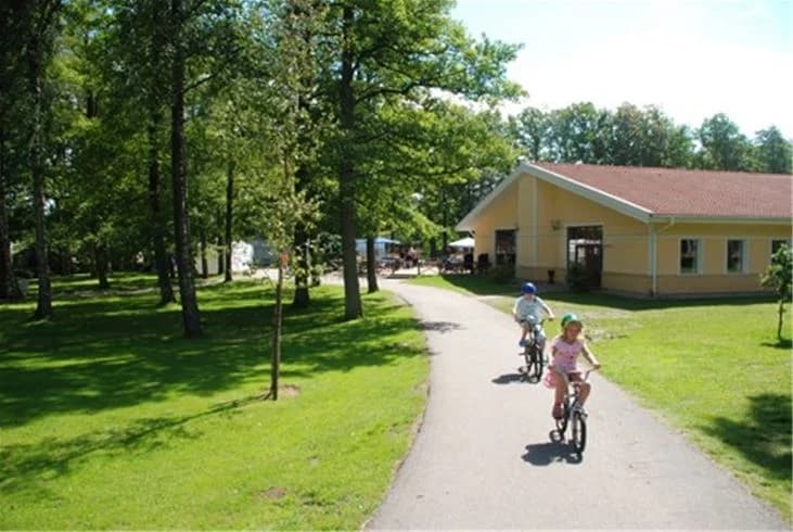 En cykel står parkerad under ett träd på Gullbrannagårdens rekreationsområde, omgivet av grönska och friluftsliv.