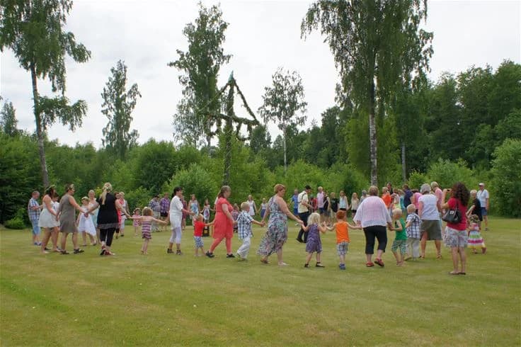 En grupp människor engagerade i fritidsaktiviteter vid Otterbergets bad och camping, omgivna av träd och vårgrönska, skapar en livlig och social atmosfär.