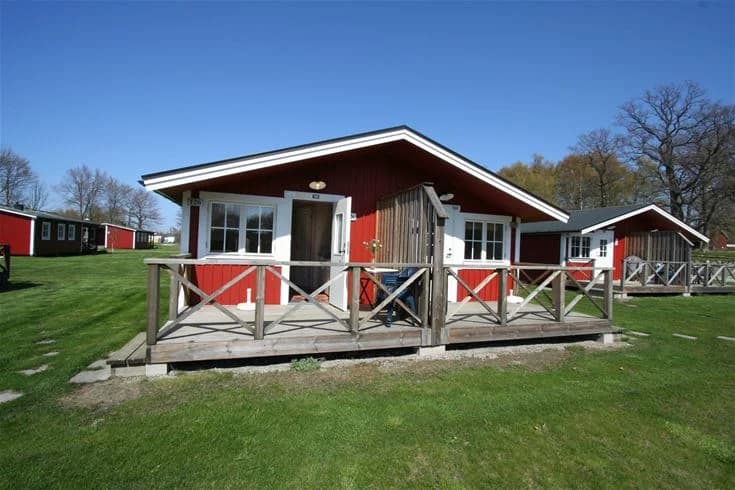 En mysig stugby på Saxnäs camping med gröna gräsmattor, fritidsaktiviteter och tältplatser i skuggan av stora träd.
