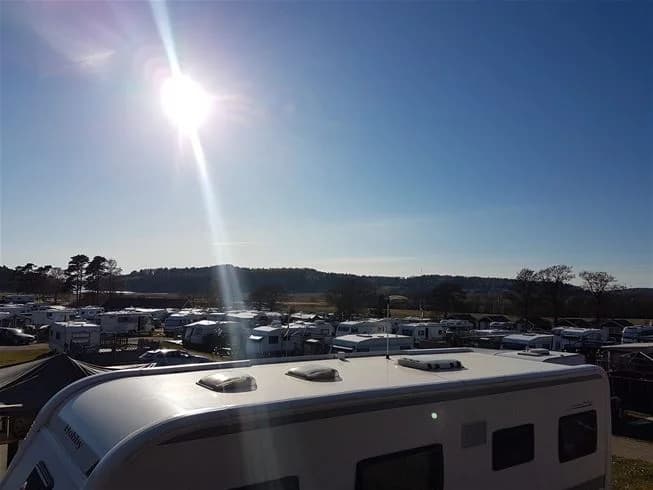 En husvagn och husbil som står parkerade på en camping vid skymning, med en vacker solnedgång i bakgrunden.