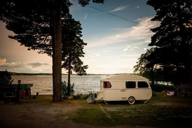 En campingplats vid Bredsands bad & camping med flera husvagnar och husbilar parkerade i närheten, omgiven av gröna träd och en klar himmel.