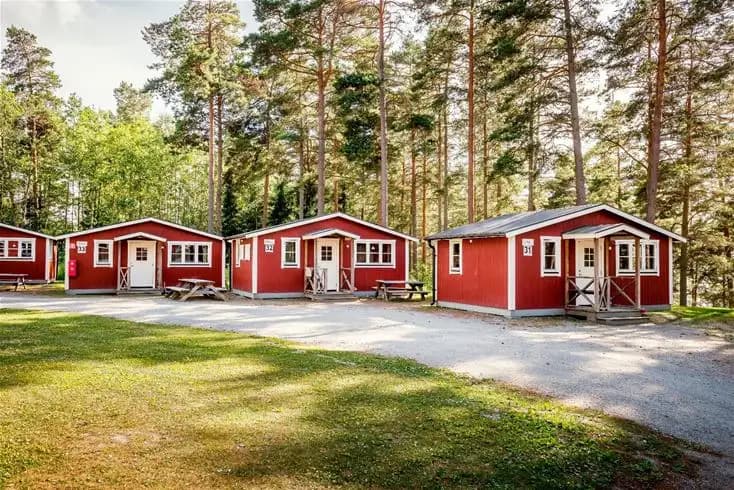 En mysig timmerstuga omgiven av skog, belägen vid Bredsands bad & camping, med en grön trädgård och rustik charm.