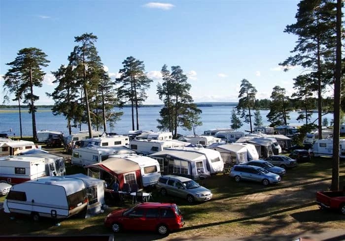 Vy över Karlsborgs camping med kustlinje där sandstranden möter det blå havet, omgivande grönska och en lång brygga som sträcker sig ut i vattnet.
