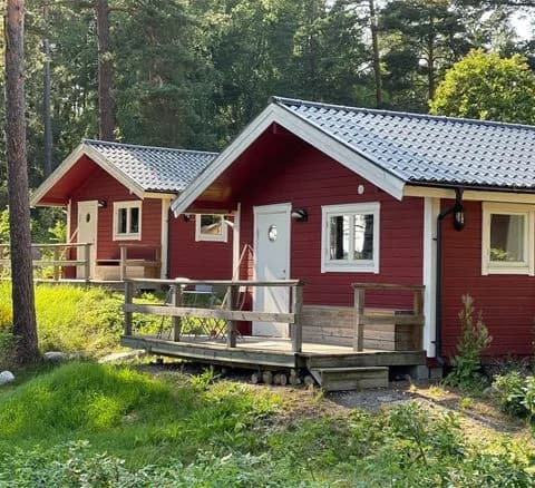 En bild av en mysig stuga i trä med en grönskande trädgård, belägen på Waxholms camping.