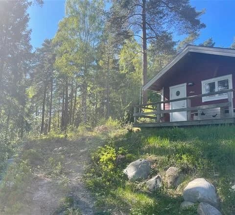 En pittoresk trästuga omgiven av grönska och skog på Waxholms camping, viskar om lantlig charm och avkoppling nära naturen.