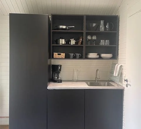 En hemtrevlig och välorganiserad köksinredning med ljusa skåp, hyllor och moderna köksapparater på Waxholms camping.