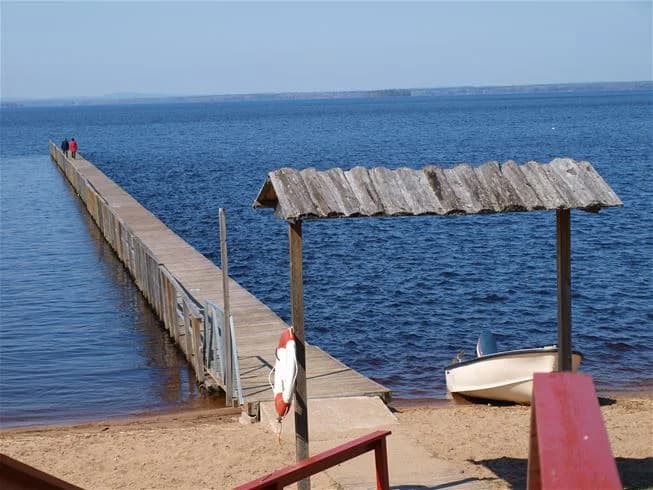 En bild av Årsunda strandbad som visar en träbrygga som sträcker sig ut i havet. Omkring bryggan syns den kustnära omgivningen, med träplankor som skapar en promenadväg längs stranden. Det avbildade området framhäver den natursköna kustlinjen och det klara vattnet.