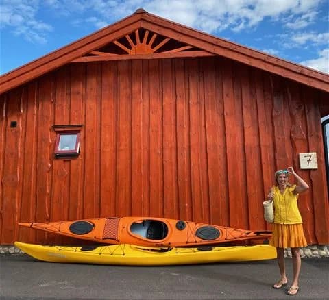 En person paddlar en kajak på en lugn sjö vid Torsby camping, omgiven av vacker natur och spegelblankt vatten.