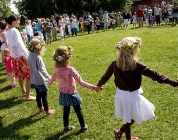En grupp människor i fritidskläder som njuter av en vårdag utomhus på Askeviks camping & stugor. Barn och vuxna deltar i olika aktiviteter, omgivna av grönskande natur.