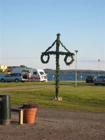 En blå himmel med några moln i bakgrunden. I förgrunden syns en trästolpe med en religiös symbol i form av ett kors. Platsen är en del av Västra Kajen Camping.