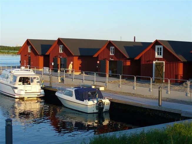 En solig dag vid en marina med flera båtar förtöjda längs bryggorna vid Västra Kajen camping. Vattnet reflekterar himlen och båtarna, och skapar en lugn och inbjudande atmosfär.