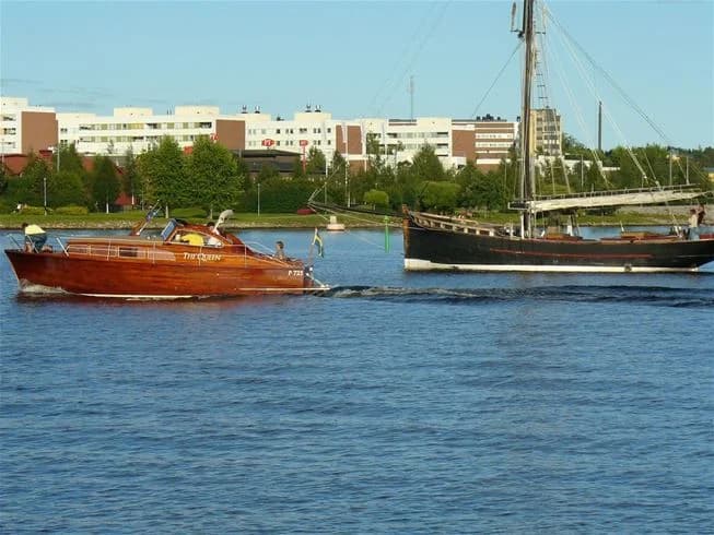 En segelbåt ligger förtöjd vid en brygga på Västra Kajen Camping, mot en bakgrund av hav och klarblå himmel.