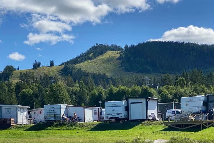 En naturskön campingplats omgiven av träd och kullar på Kläppens camping, med husbilar och ett öppet fält i en dalgång.