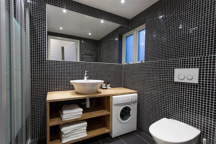 Ett modernt badrum på Hölick Havsresort med stilren inredning. Rummet har vita kaklade väggar, klinkergolv, ett handfat och en stor spegel.