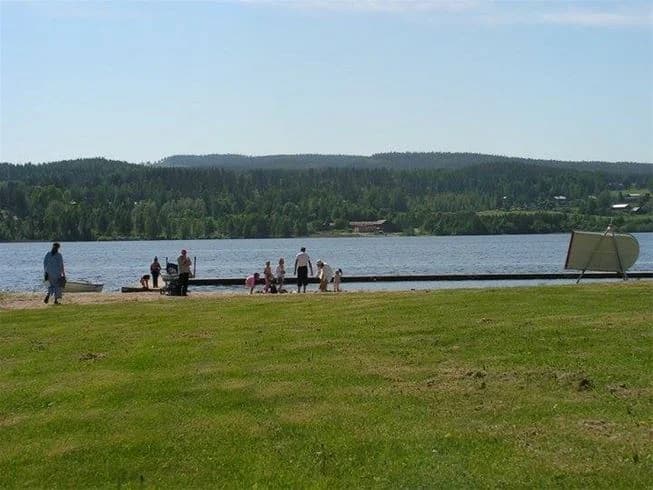 Bilden visar en naturskön sommarvy vid Borgsjö strand. I förgrunden finns en utomhusbänk omgiven av grönska, där besökare kan njuta av fritid och rekreation. I bakgrunden syns ett vattenreservoar, typiskt för ett sjöområde, vilket förstärker semester- och semesterortsatmosfären.
