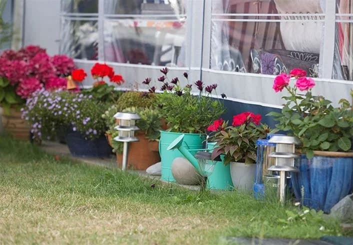 Blomstrande trädgård med olika växter och blomkrukor, grönska i bakgrunden på Borrbystrand Camping under vårtid.