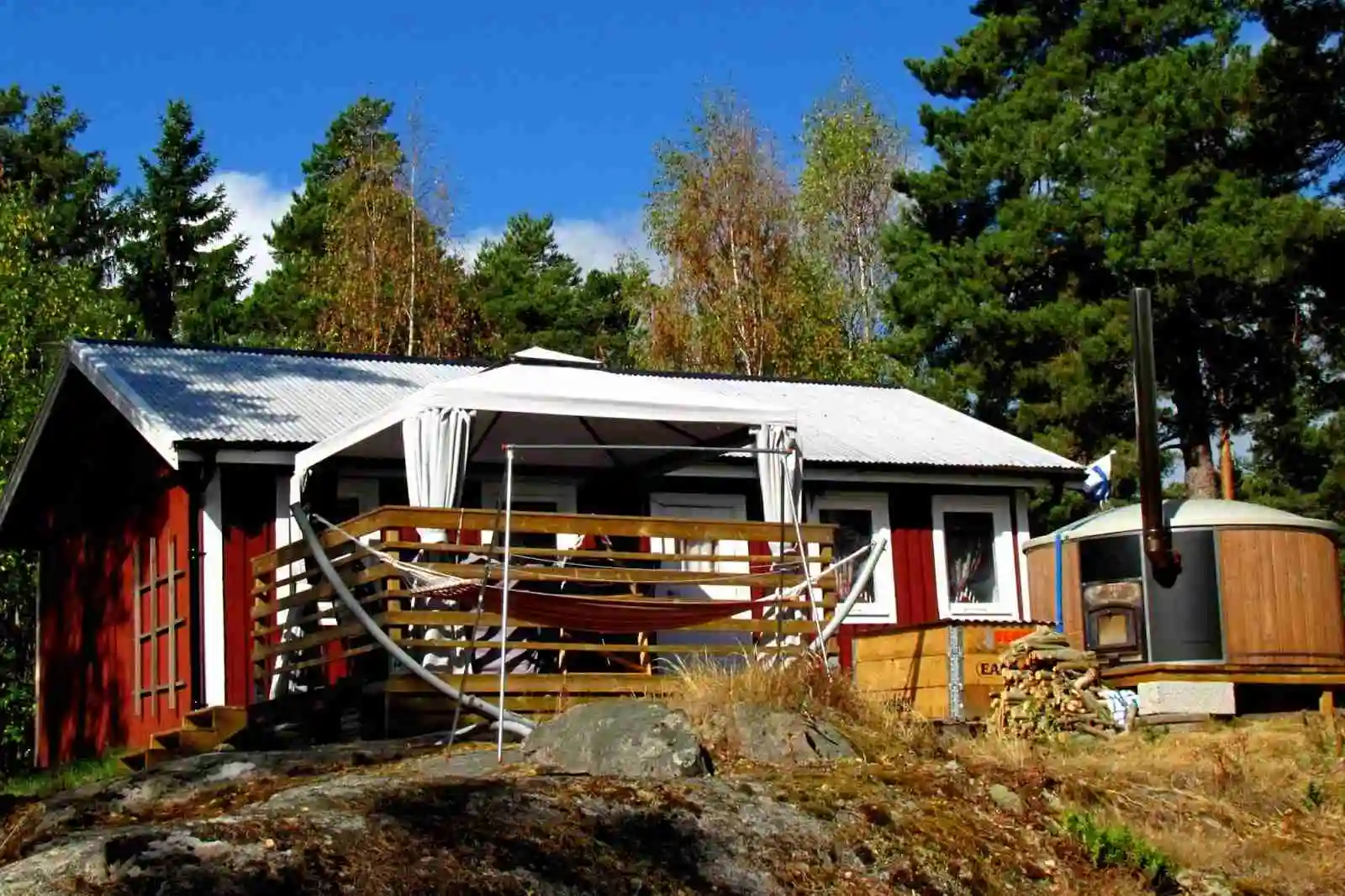 Bild på Arkösunds camping med en timmerstuga omgiven av träd i en lantlig miljö. Stugan ligger i skuggan och omringas av grönska.