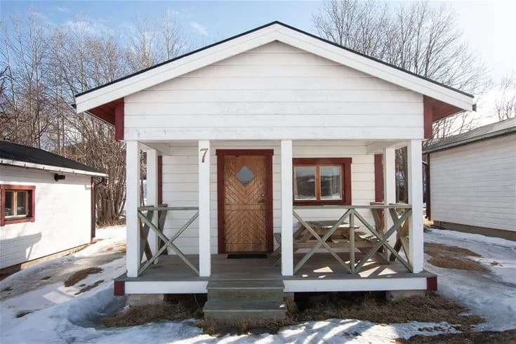 Bild av en trästuga på Rätans camping med en träfasad och en dörr. Stugan har trappsteg vid ingången och är omgiven av naturlig grönska.