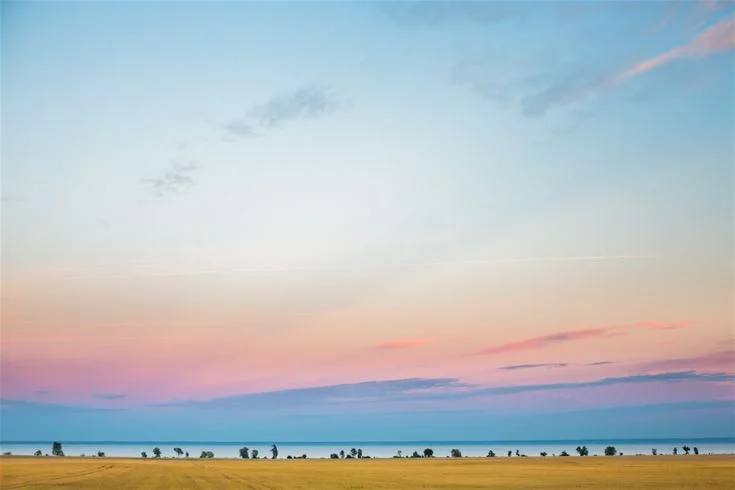 En vidsträckt himmel i skymningen med orange och blå toner, moln och en horisont över en vidsträckt slätt vid Breviks camping & ställplats.