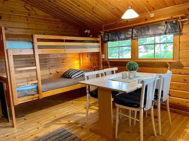 Bild av insidan av en timrad stuga vid Norråkers camping. Rummet har trägolv och trätak, inrett med rustika trämöbler. Atmosfären är varm och inbjudande, perfekt för en avkopplande vistelse.