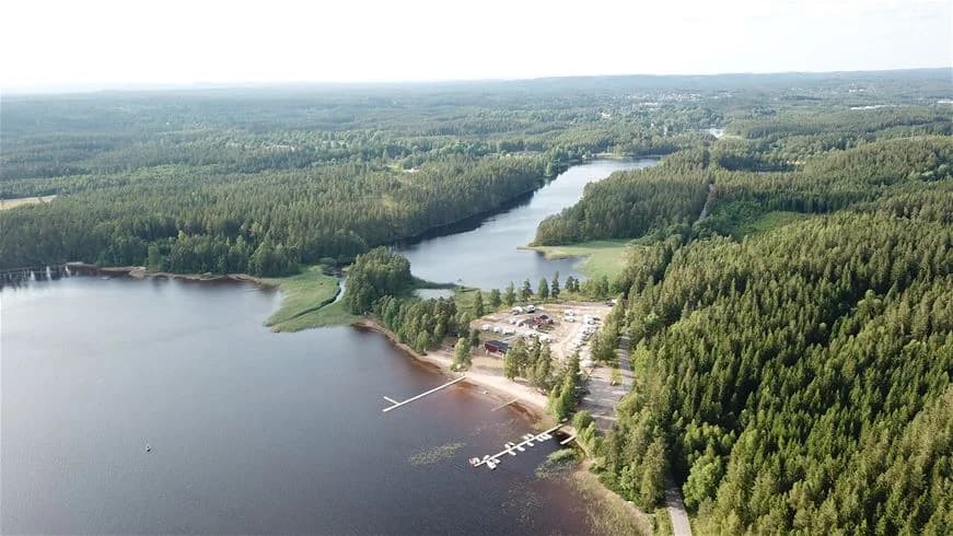 En stilla sjö omgiven av grönskande träd vid Gnosjö strand, där naturen möter vattnet i en avkopplande miljö.