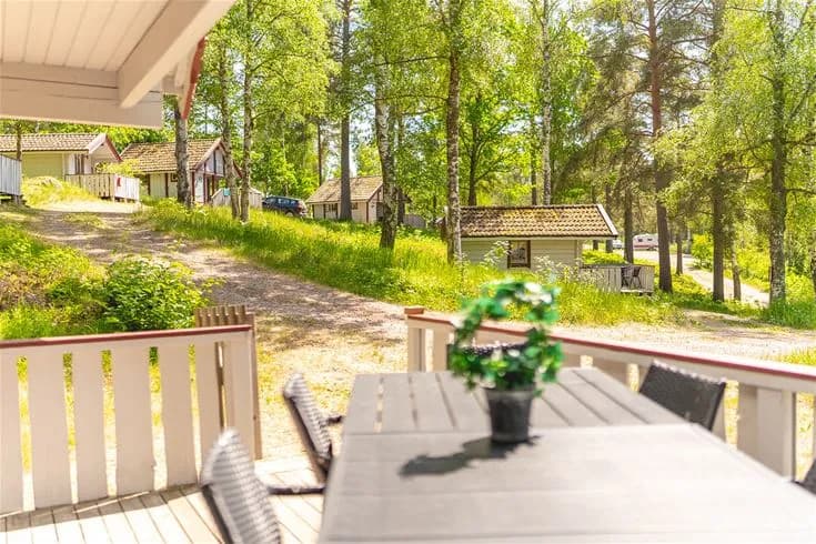 En mysig stuga vid Vimmerby camping, omgiven av trä och gröna ytor, med en liten veranda och trädgård.