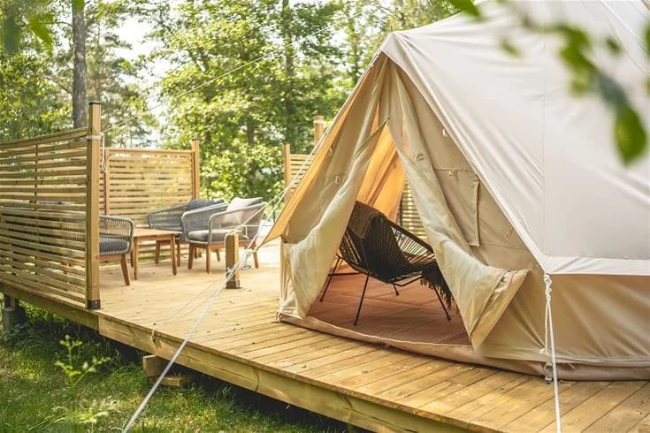 Bild av Vimmerby camping - Nossenbaden: En skuggig campingplats med tält och utomhusmöbler, omgivet av vacker trämiljö och ett trädäck där besökare kan njuta av fritidsaktiviteter.