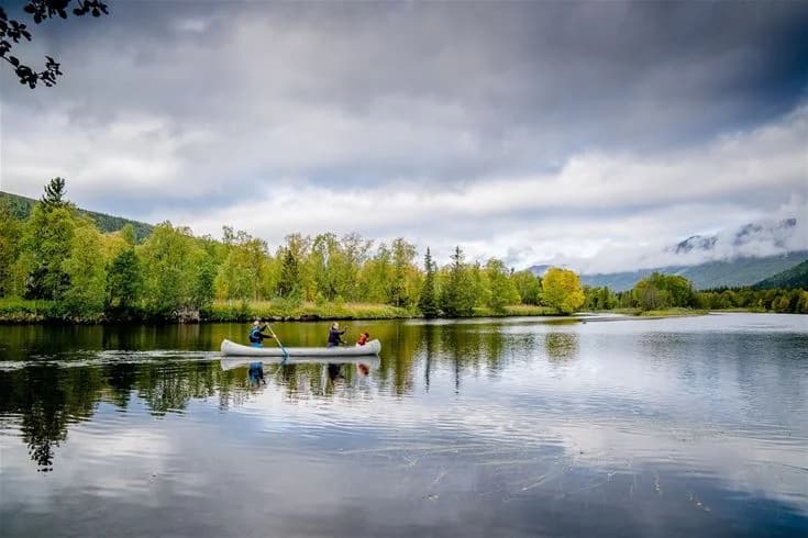 En roddbåt flyter stilla på en klar sjö omgiven av grönskande natur vid Camp Kittelfjäll. Vattnets yta speglar omgivningen i den avkopplande och naturnära miljön.