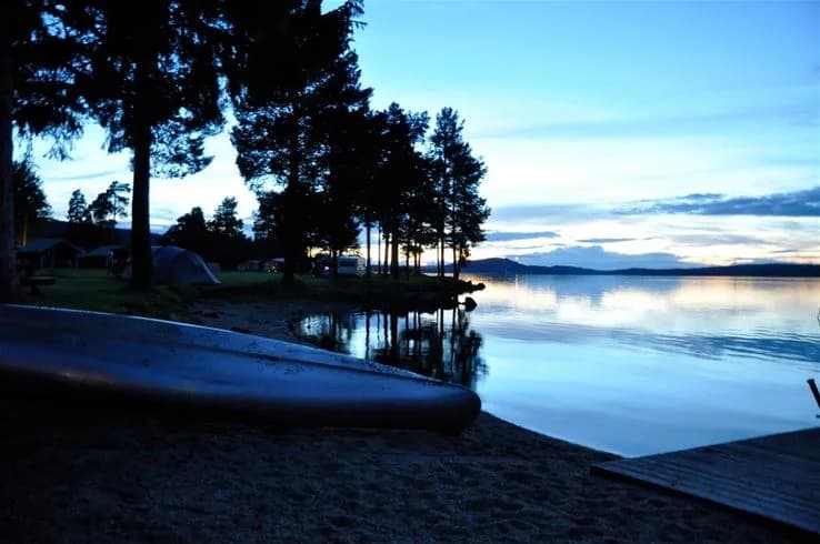 Bild av en fridfull sjö under skymningen, där det blåa vattnet reflekterar himlen. I bakgrunden sträcker sig horisonten och bildar en rogivande naturvy vid Camp Viking.