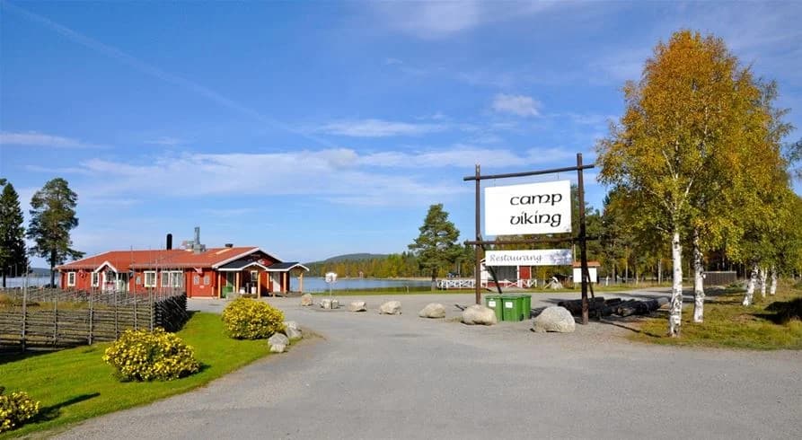 En lantlig stuga på en tomt med grönska, omgiven av öppna fält och några stolpar, med en pittoresk atmosfär som skapar en idyllisk miljö vid Camp Viking.