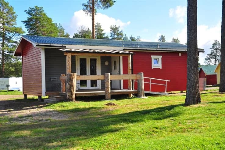 En charmig timmerstuga med träfasad och en enkel dörr, omgiven av skogslandskap. Perfekt för den som söker en rustik och avkopplande vistelse i naturen.