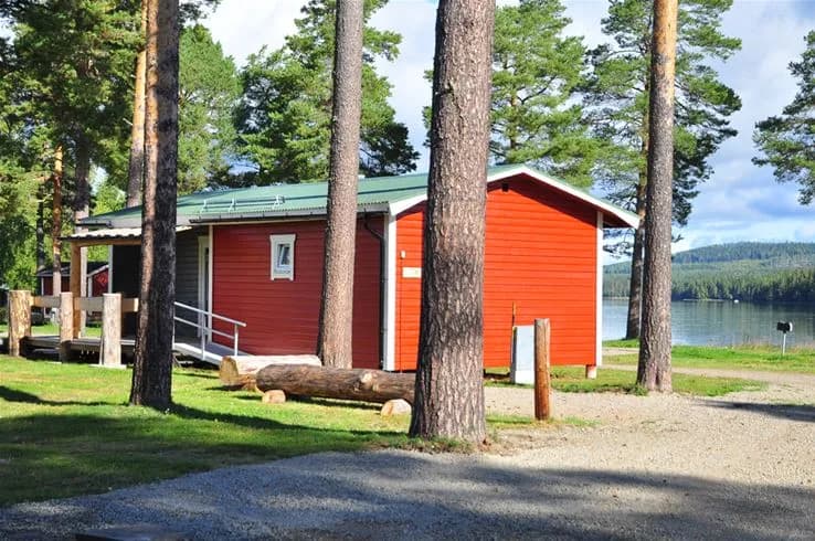 En mysig timmerstuga i skuggigt trälandskap, omgiven av grönska, vid Camp Viking.