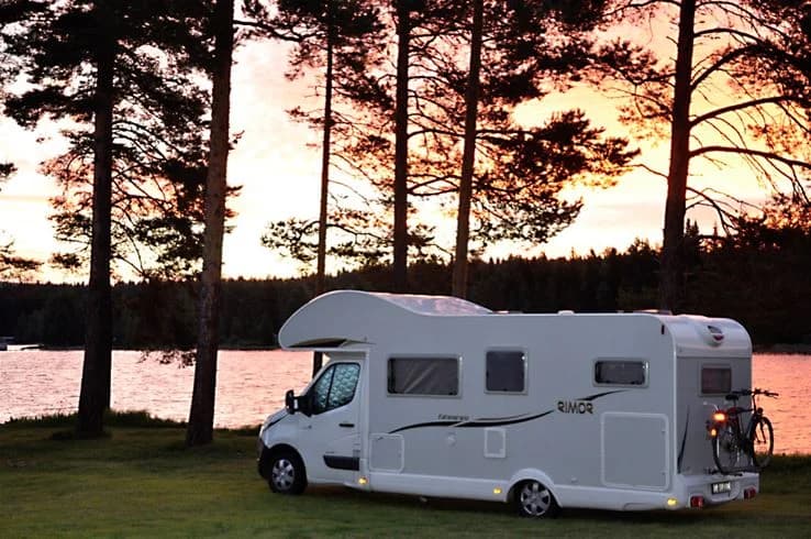 En husvagn med öppna dörrar på en campingplats omgiven av träd, representerar friluftslivet på Camp Viking.