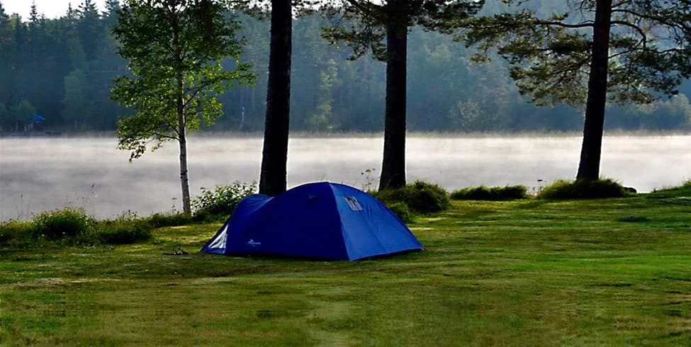 En stillsam campingplats vid Camp Viking, omgiven av tät skog och en sjö. Tält står uppställda under skyddande presenningar, idealiska för utomhusaktiviteter och avkoppling i naturen.