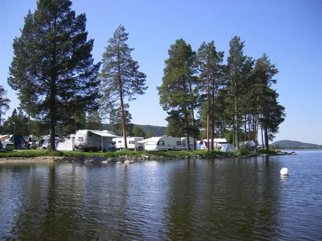 Vy över ett naturskönt vattendrag vid Camp Viking, omgivet av gröna stränder och skogsklädda områden, med spegelblanka vattnet under en klar himmel.