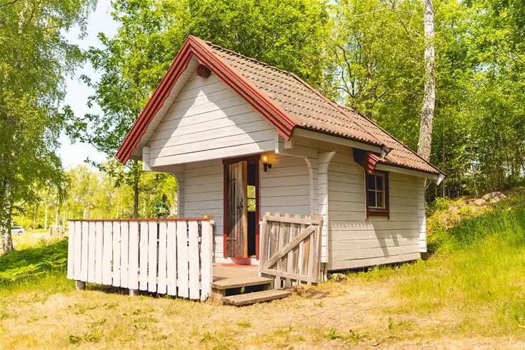 En trästuga med rött tak på Vimmerby Camping - Nossenbaden, omgiven av grönska i ett lantligt och rofyllt område.
