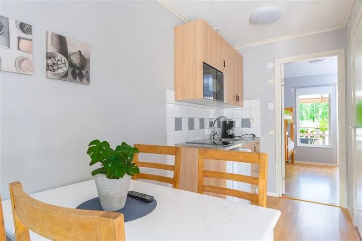 En interiörbild av en stuga på Vimmerby Camping - Nossenbaden. Rummet har trägolv och träväggar. Det finns möbler som stolar och bord, och en dörr syns i bakgrunden.