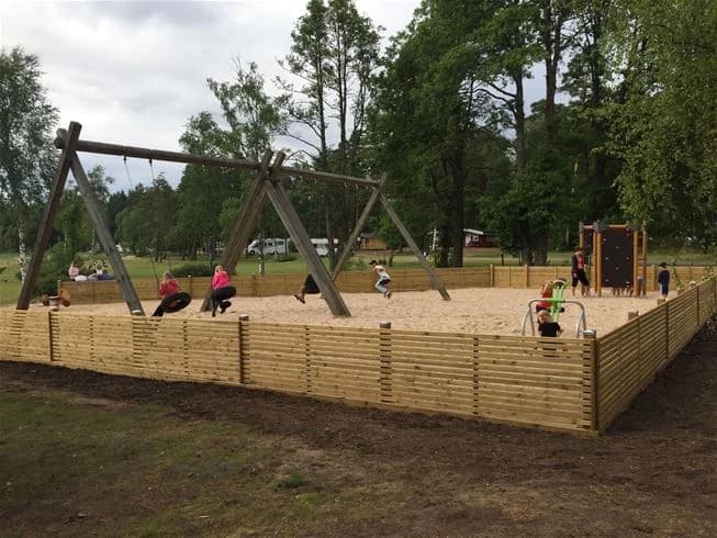 En lekplats omgiven av träd på Flatens camping med olika utomhuslekredskap för rekreation och nöje.