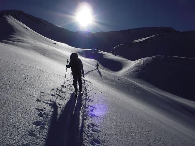 En snötäckt campingplats i Åre med imponerande bergslandskap i bakgrunden. Flera vinterentusiaster ses åka skidor och använda skidutrustning, omgivna av den vinterliga naturen.