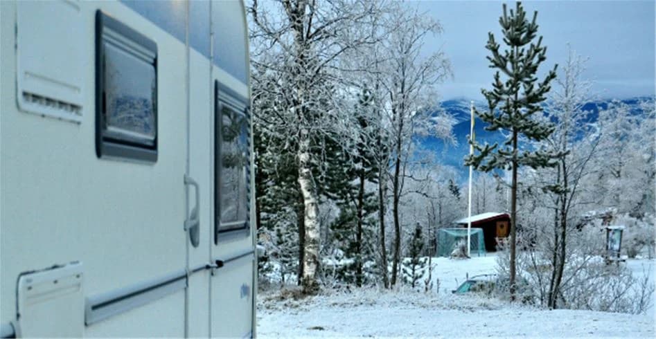 En husvagn täckt av snö vid en vintercamping i Åre, omgiven av frusna träd och ett snötäckt landskap. En stjärnklar natthimmel lyser upp den frostiga miljön.