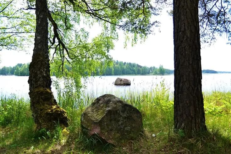 En naturskön plats vid en sjö med klara vatten och gröna omgivningar och stenar vid strandkanten, fångar den fridfulla atmosfären av Gökaskratts camping.