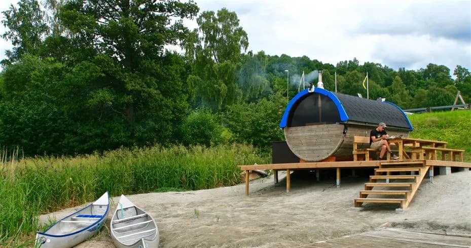 En bild som visar en båt vid strandkanten på Skotteksgården Camping & Stugby, omgiven av grönska och vatten.