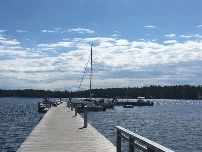 Ett lugnt vattendrag sträcker sig mot horisonten under en klarblå himmel. I vattnet syns flera båtar i olika storlekar, vilket antyder en populär plats för båtliv. Den öppna och vidsträckta utsikten ger en känsla av fridfullhet och avkoppling, typiskt för Stenö havsbad & camping.