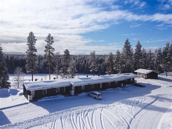 En snötäckt stuga omgiven av frostiga landskap vid Åsarna Skicenter, med glaciärliknande former och lärkträd i bakgrunden under en kall vinterdag.