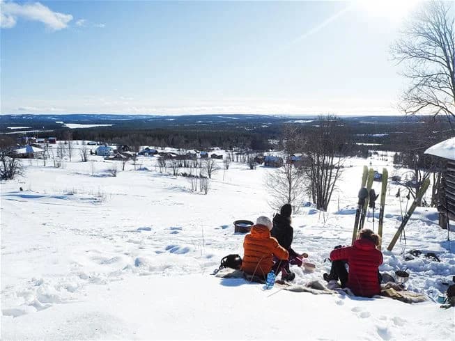 En grupp människor som njuter av vintern och leker i snön vid Åsarna Skicenter. Snötäckta backar och frostiga träd utgör bakgrunden.