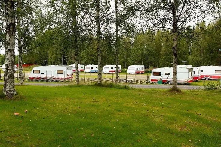 En bild som visar en rad uppställda husbilar och husvagnar vid Åsarna skicenter. Fordonen står parkerade på en grusad yta omgivna av grönska, vilket indikerar att det är en campingplats.