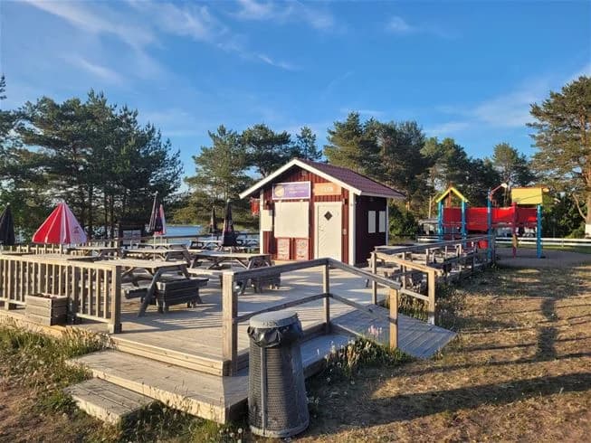 En campingplats vid Älvkarleby med picknickbord och parkbänkar i skuggan, omgiven av öppna ytor för rekreation och avkoppling.