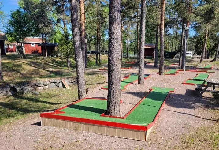 Bild av Älvkarleby Fiskecamping med välskött gräsmatta och trädgårdslandskap. Golfbana i miniatyrformat syns på konstgräs, omgiven av grönska och parkmiljö.